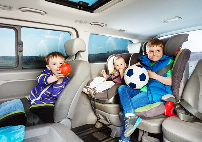Three little boys, age-diverse brothers, travelling by car in safety seats, snacking and playing ball during the trip